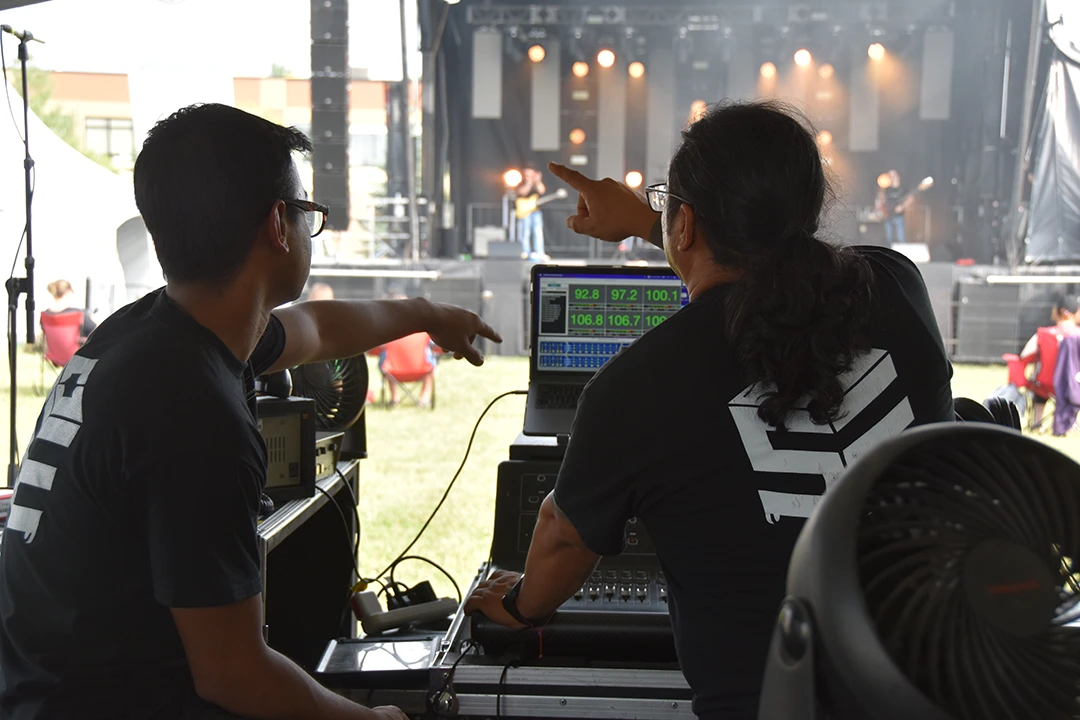 Two OSE crew members work with high-tech audio equipment while setting up for an outdoor concert