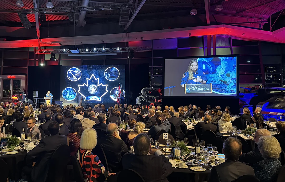 A Canadian astronaut speaks to gala attendees from a lit-up stage and large video screens at the Royal Canadian Geographical Society's Geographica dinner.