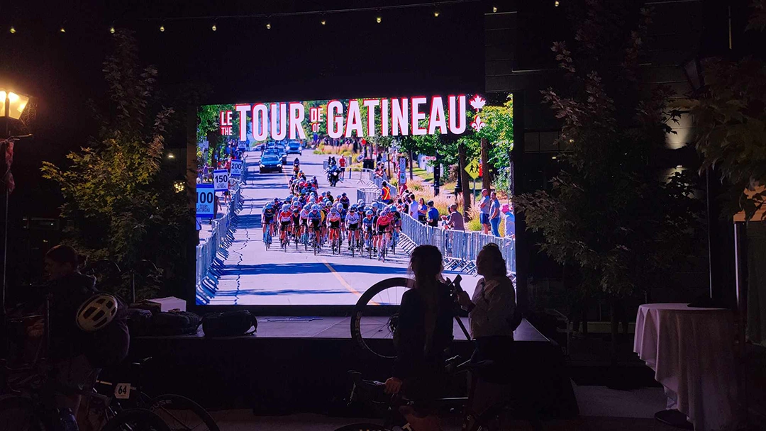 A lit up video screen at night showcases the day's Tour de Gatineau performance
